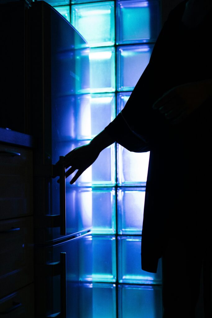 A silhouette of a person opening a fridge in a neon-lit kitchen, creating a modern atmospheric scene.